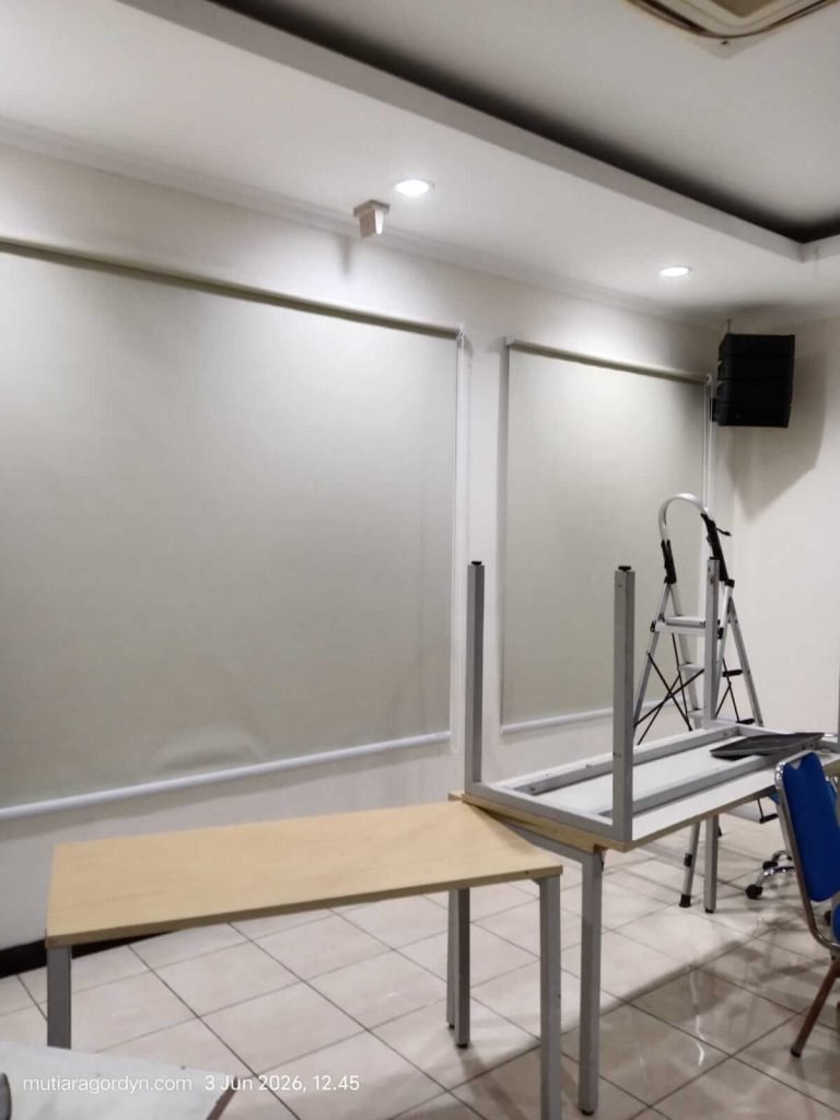Pemasangan Roller Blind jenis Blackout warna abu-abu minimalis untuk ruang kerja ruko, memberikan perlindungan total dari terik matahari luar